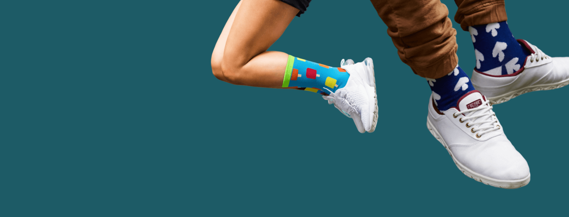 Two pairs of legs wearing colorful socks and white sneakers against a light blue background